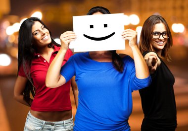 Young friends holding a happy emoticon at city by night clipart