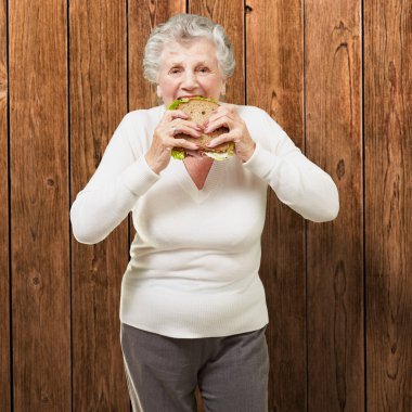 Portrait of senior woman eating vegetal sandwich against a woode clipart