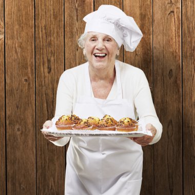 Senior vrouw cook een dienblad met muffins houden tegen een houten b