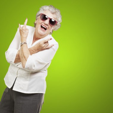 Portrait of senior woman doing rock symbol over green background clipart