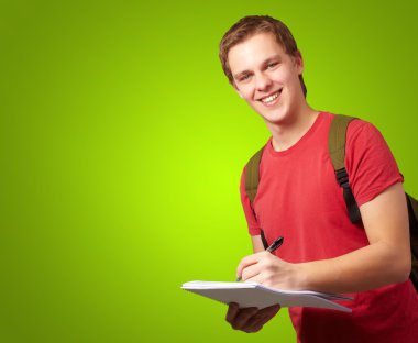 Portrait of young student man writing on a notebook over green b clipart