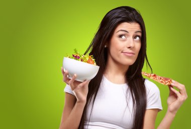 Portrait of young woman choosing pizza or salad against a green