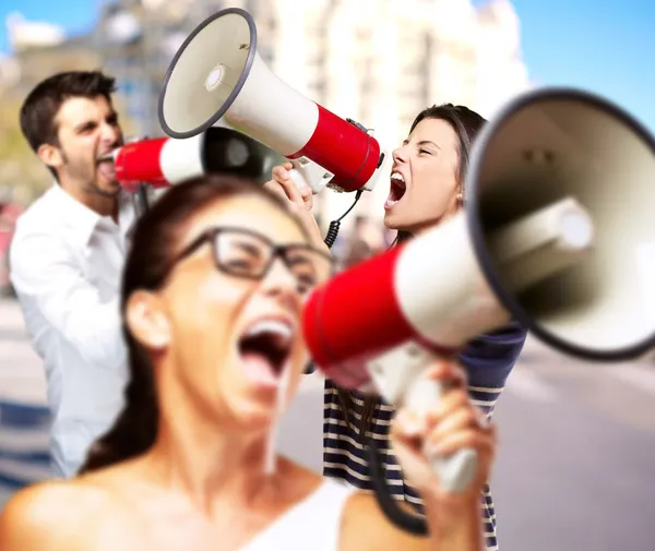 Jovens amigos gritando com megafone contra um edifício — Fotografia de Stock