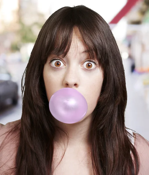 stock image Young girl with a pink bubble of chewing gum against a street ba
