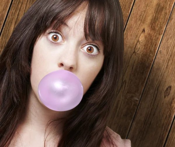 Chica joven con una burbuja rosa de goma de mascar contra una ba de madera — Foto de Stock