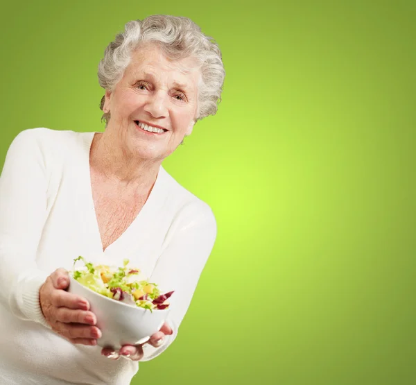 Portrait of senior woman showing a fresh salad over green backgr — Stock Photo, Image