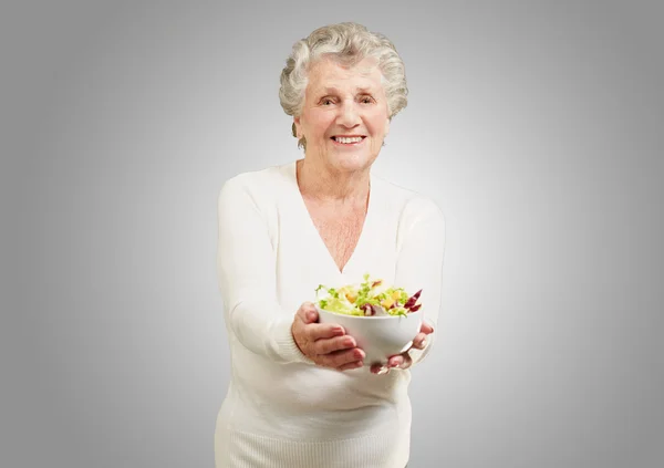 Retrato de mujer mayor mostrando una ensalada fresca sobre fondo gris —  Fotos de Stock