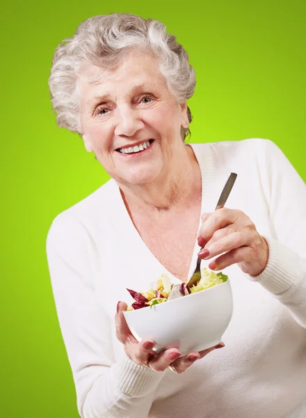 吃沙拉在绿色背景的高级女人的画像 — 图库照片