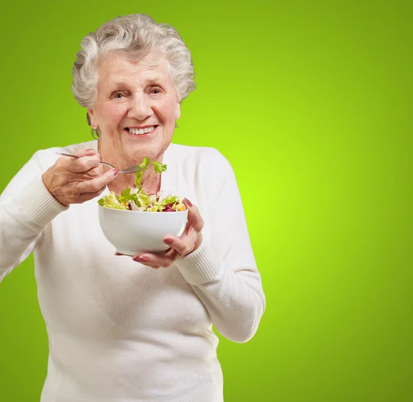 Portrait of senior woman eating a fresh salad over green backgro — Stock Photo, Image