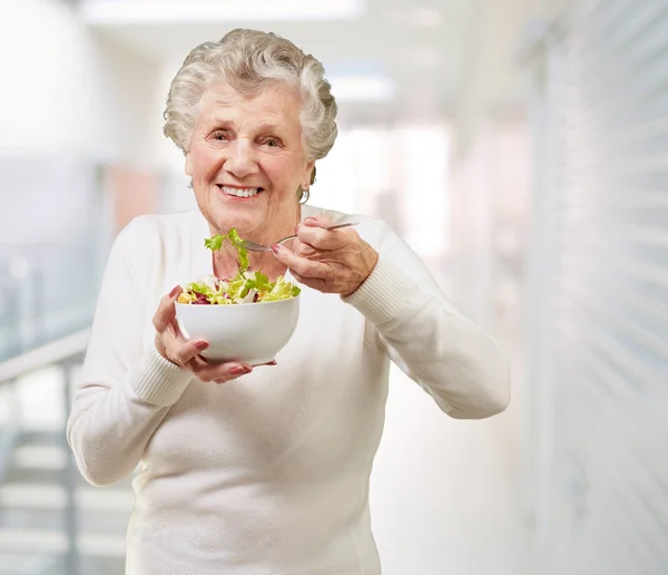 Ritratto di una donna anziana che mangia un'insalata fresca nell'edificio moderno — Foto Stock
