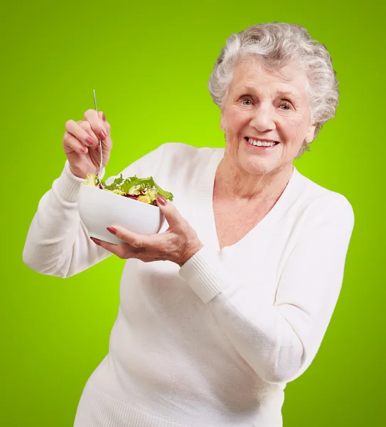 Portret senior kobiety jedzenie sałatka na zielonym tle — Zdjęcie stockowe