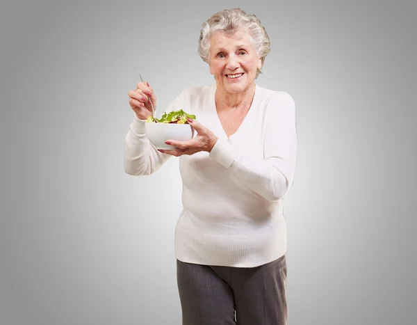 Portret senior kobiety jedzenie sałatka na szarym tle — Zdjęcie stockowe
