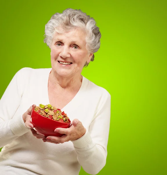 Portrait of healthy senior woman holding cereals bowl over green — Stock Photo, Image