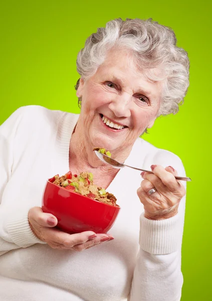 Portrait of senior woman holding a cereals bowl against a green — Stock Photo, Image