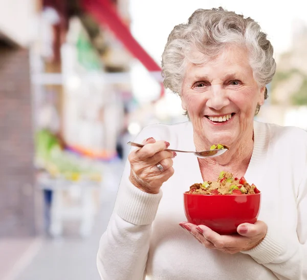 Portrait d'une femme âgée tenant un bol de céréales contre un légume — Photo