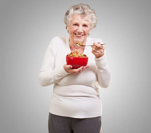 Portrait of senior woman holding a cereals bowl against a grey b — Stock Photo, Image
