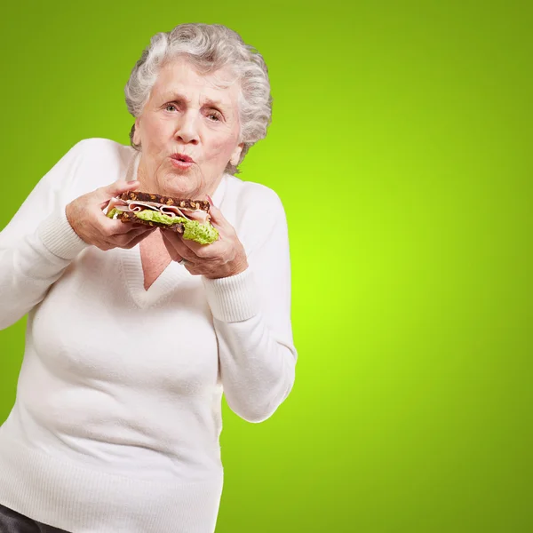 Retrato de mulher idosa segurando um delicioso sanduíche sobre verde — Fotografia de Stock