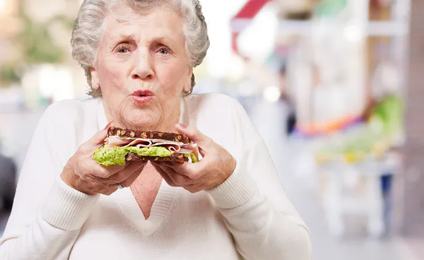 Portrét starší ženy držící lahodný sendvič na ulici — Stock fotografie