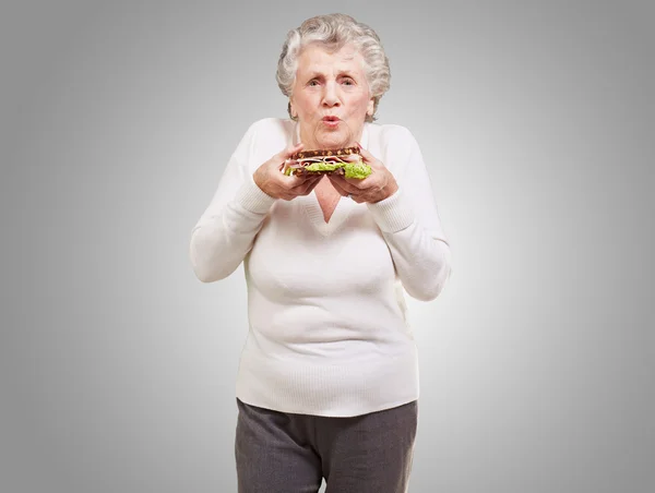 Retrato de mulher idosa segurando um delicioso sanduíche sobre cinza — Fotografia de Stock
