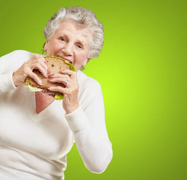 Yeşil arkaya bitkisel sandviç yeme kadın kıdemli portresi — Stok fotoğraf