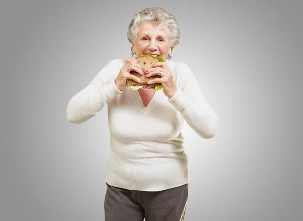 Portrét starší ženy jíst rostlinné sendvič nad šedé pozadí — Stock fotografie
