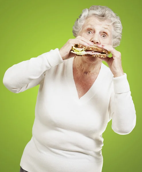 Mulher sênior comendo um sanduíche saudável contra um backgroun verde — Fotografia de Stock
