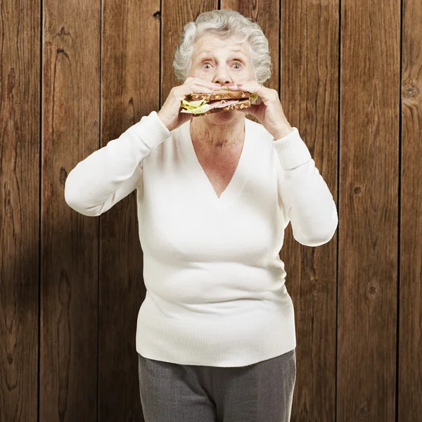 Ahşap backgrou karşı sağlıklı bir sandviç yeme kadın kıdemli — Stok fotoğraf