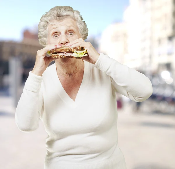 Donna anziana mangiare un panino sano contro un backgrou strada — Foto Stock