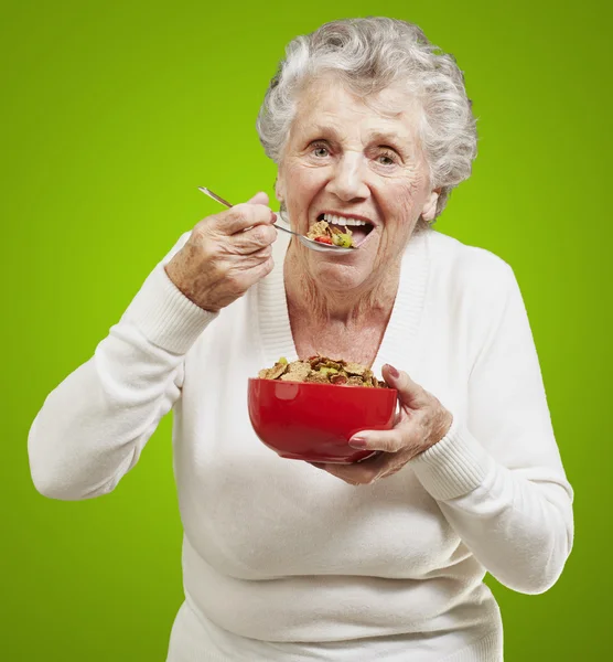 Senior mulher comendo cereais de uma tigela vermelha contra um ba verde — Fotografia de Stock