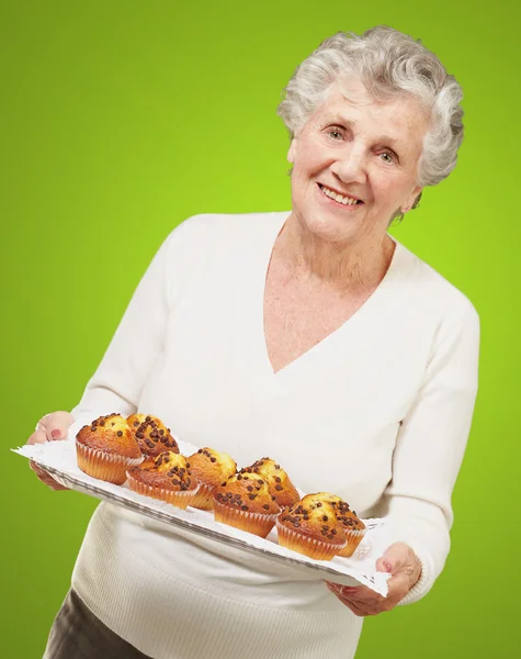 Ritratto di donna anziana che mostra muffin fatti in casa sopra il verde — Foto Stock