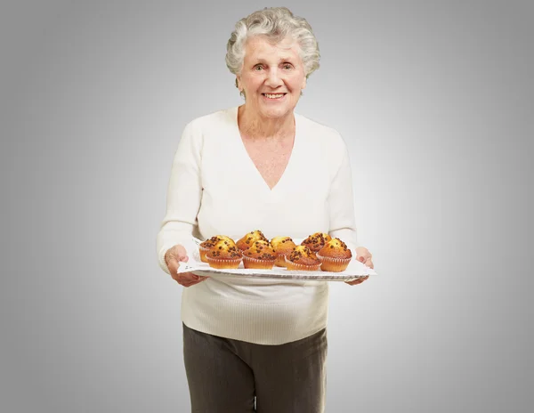 Ritratto di donna anziana che mostra muffin fatti in casa su grigio — Foto Stock