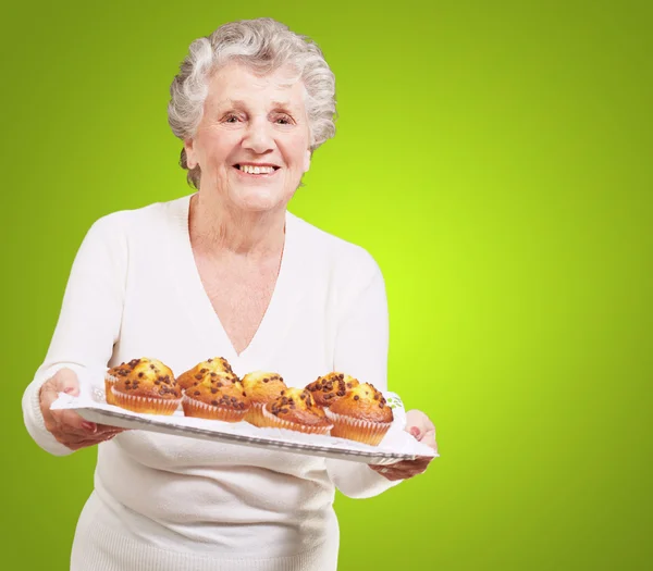 Portrait of senior woman showing a chocolate muffin tray over gr — Stock Photo, Image