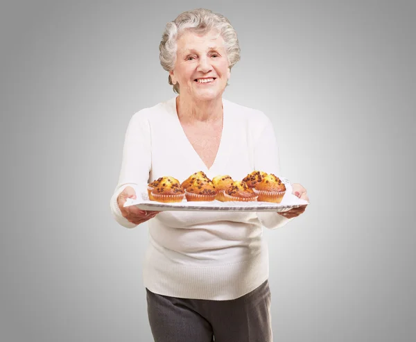 Portrait of senior woman showing a chocolate muffin tray over gr — Stock Photo, Image