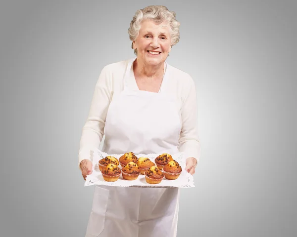 Retrato da cozinheira idosa segurando uma bandeja de muffins de chocolate o — Fotografia de Stock