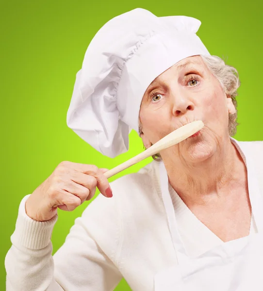 Portrait of cook senior woman with wooden spoon on mouth over gr — Stock Photo, Image