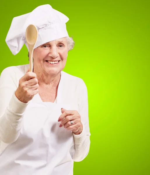 Портрет старшої кулінарної жінки, що тримає дерев'яну ложку над зеленим — стокове фото