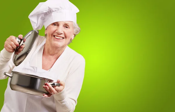 Portrait of cook senior woman opening sauce pan over green — Stock Photo, Image