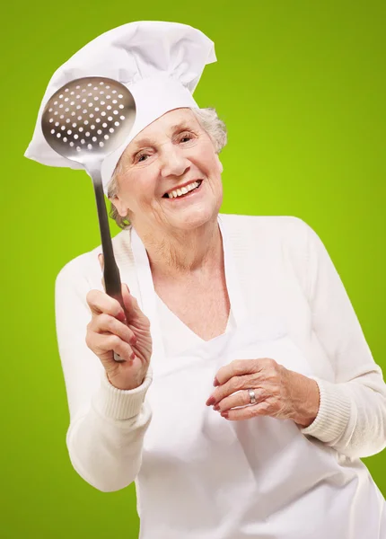 Porträt der süßen Senior-Köchin mit einem Metalllöffel über g — Stockfoto