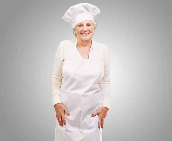 Portret kobiety starszy kucharz, uśmiechając się na szarym tle — Zdjęcie stockowe