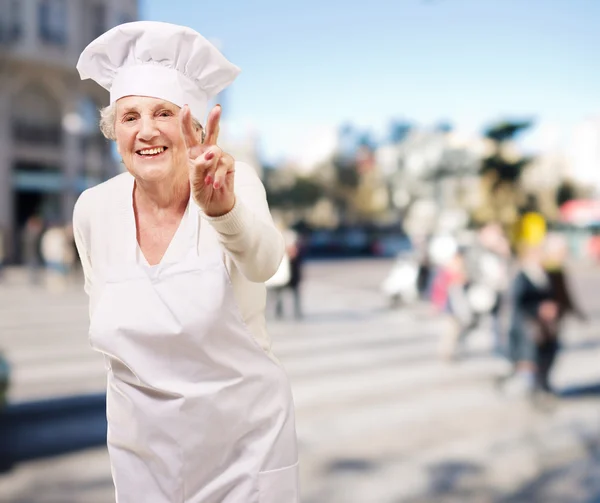 Retrato de cocinera mujer mayor haciendo buen gesto en el brillo lleno de gente — Foto de Stock
