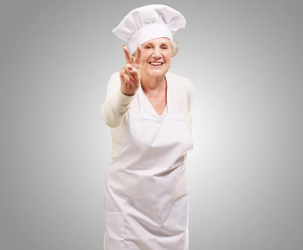 Портрет пожилой женщины-повара с одобрительным жестом над серой буквой Б — стоковое фото