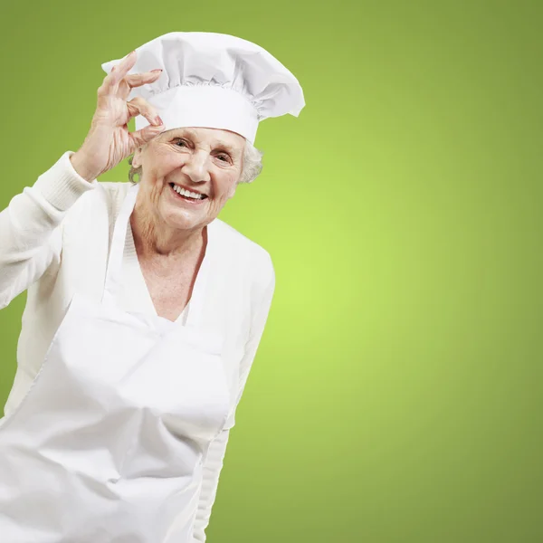 Senior-Köchin macht ein hervorragendes Symbol gegen einen grünen Rücken — Stockfoto