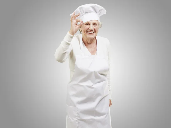 Kadın kıdemli cook gri backg karşı mükemmel bir sembol yapıyor — Stok fotoğraf