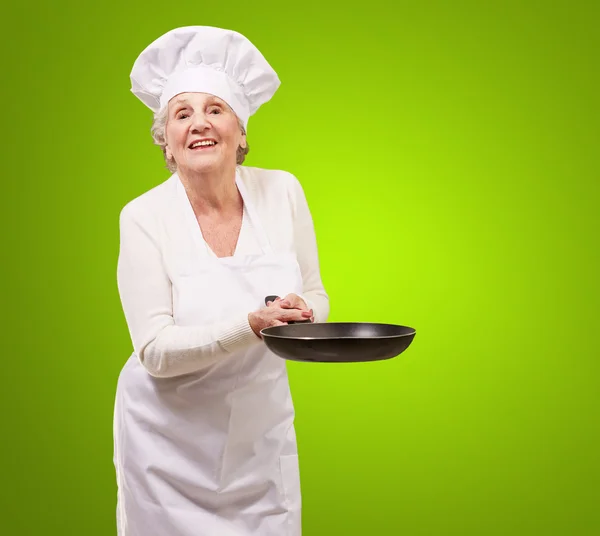 Портрет дружелюбной повара пожилой женщины, держащей сковородку над зеленью — стоковое фото