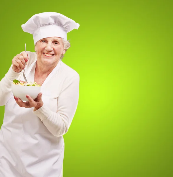 Portrait of adorable senior cook woman eating salad against a gr — Stok fotoğraf