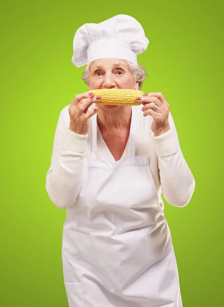 Портрет старшої кулінарної жінки, що їсть кукурудзяний коб над зеленим фоном — стокове фото
