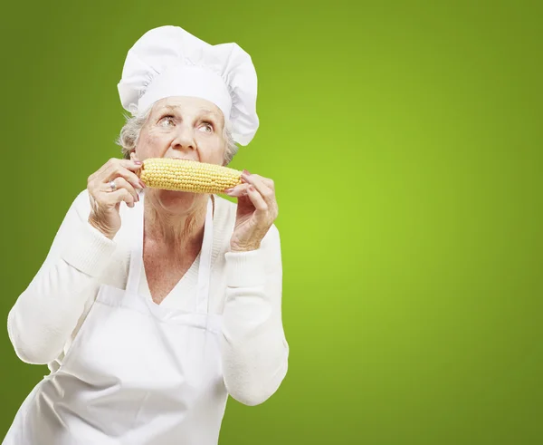 Старша жінка готує їсть кукурудзу на зеленому фоні — стокове фото