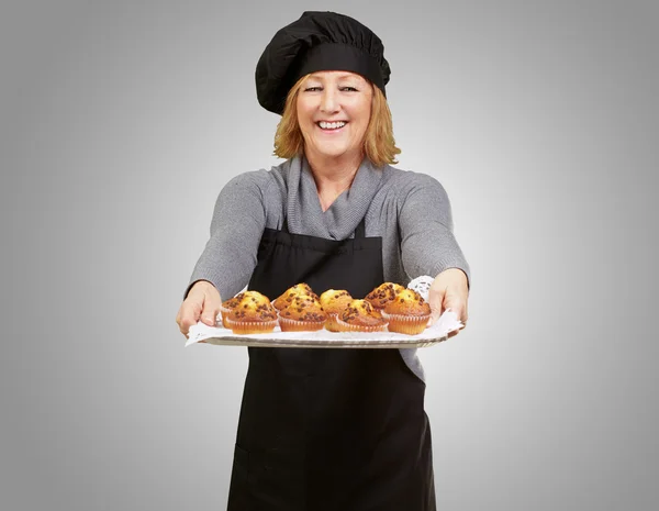 Szakács nő mutatja egy házi készítésű muffint tálca felett szürke portréja — Stock Fotó