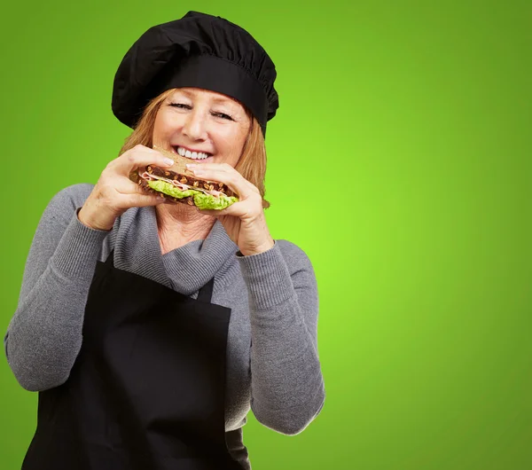 Μέσης ηλικίας γυναίκα μάγειρας κρατώντας ένα φυτικό σάντουιτς πάνω από πράσινο bac — Φωτογραφία Αρχείου
