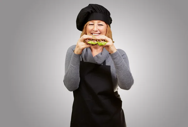 Mujer cocinera de mediana edad sosteniendo un sándwich vegetal sobre la espalda gris —  Fotos de Stock